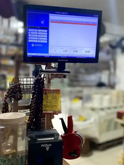 Frente de caixa Grandsoft funcionando no balcão de uma loja, com impressora de cupom e leitor de código de barras